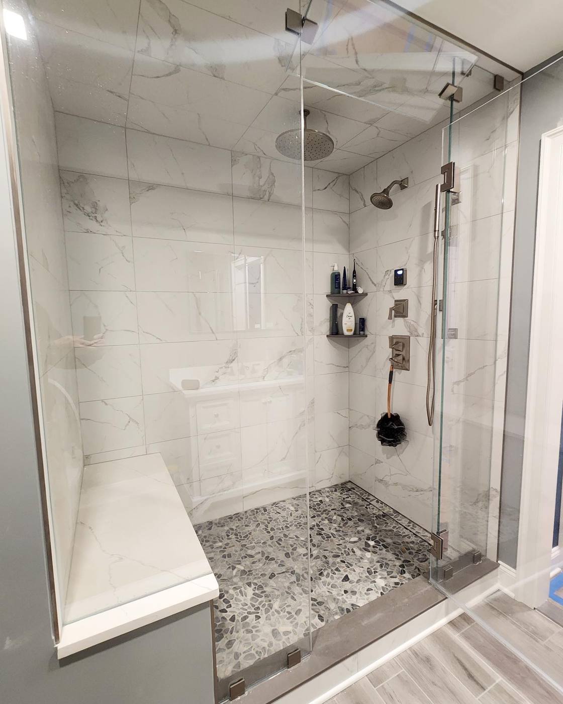 Frameless glass enclosure on a marble-look shower with bench
