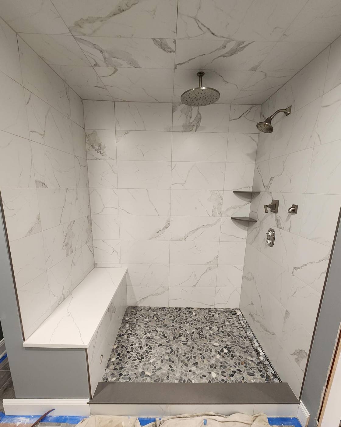 Marble-look walk-in shower with bench, dual heads and pebble floor