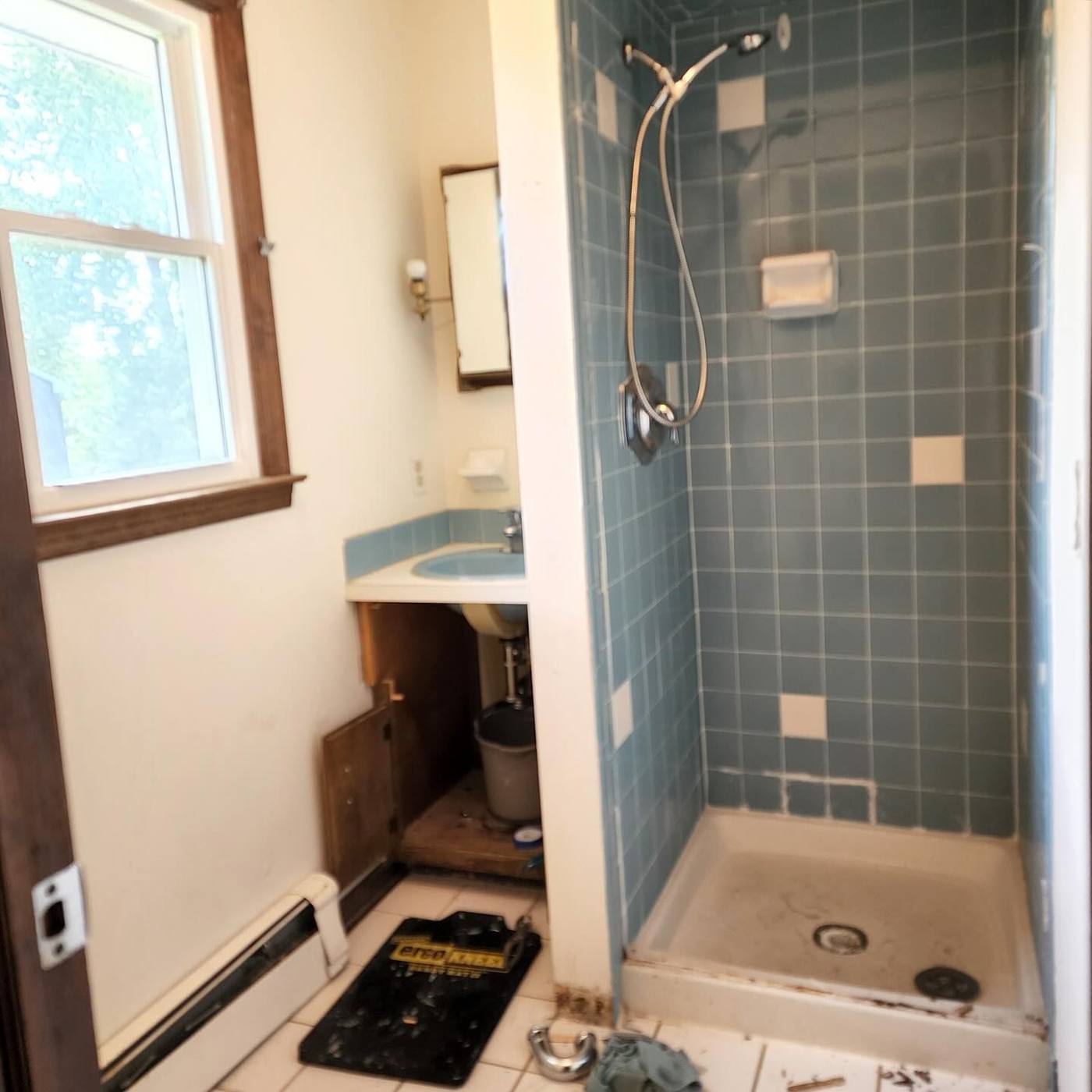 Dated small bathroom with old blue tile shower stall