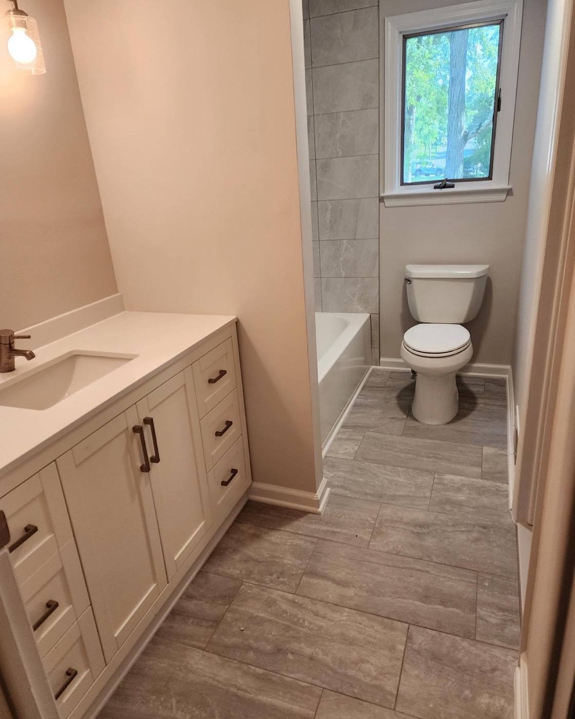 White shaker vanity and tub with wood-look tile floor